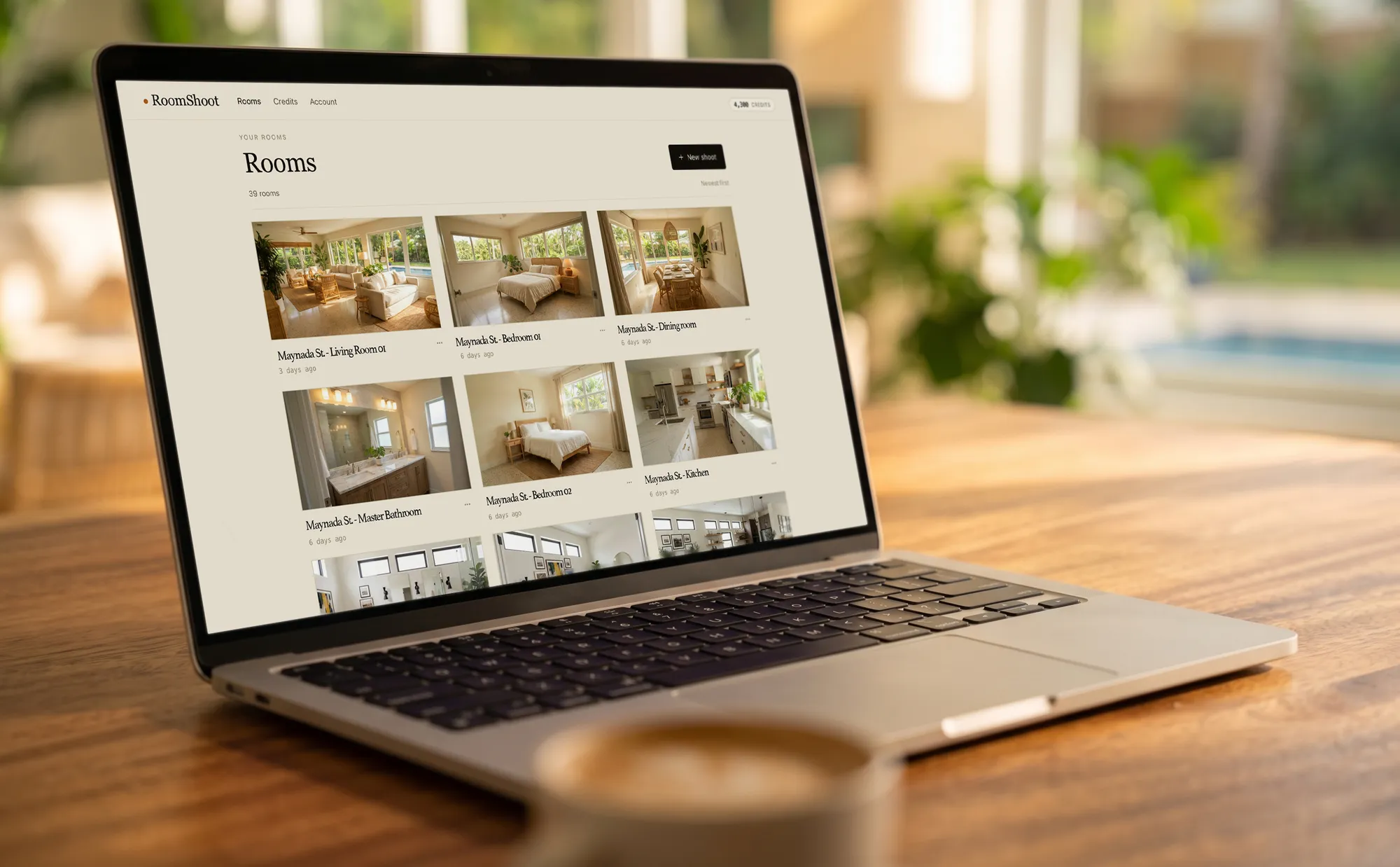 A laptop on a desk showing the RoomShoot Rooms dashboard — a grid of room thumbnails